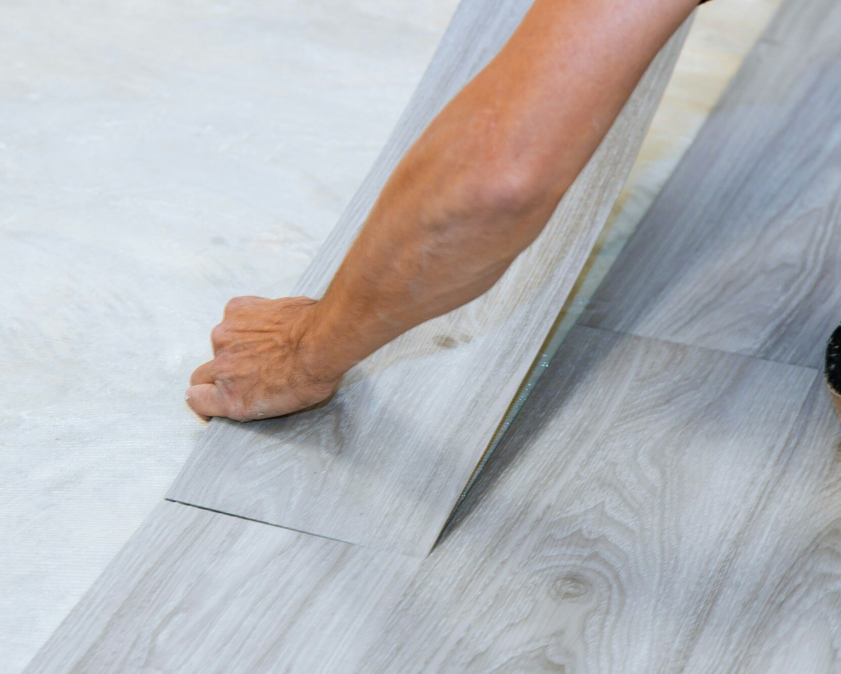 Worker installing new vinyl tile floor with new home improvement laminate wood texture floor